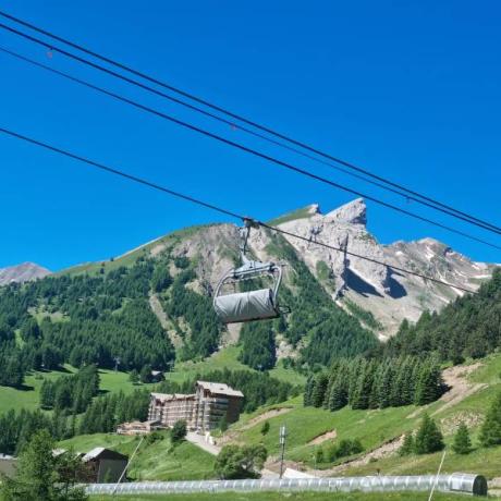 Télésiège au premier plan, paysage montagnard verdoyant avec quelques névés en altitude - Télésiège au premier plan, paysage montagnard verdoyant avec quelques névés en altitude
